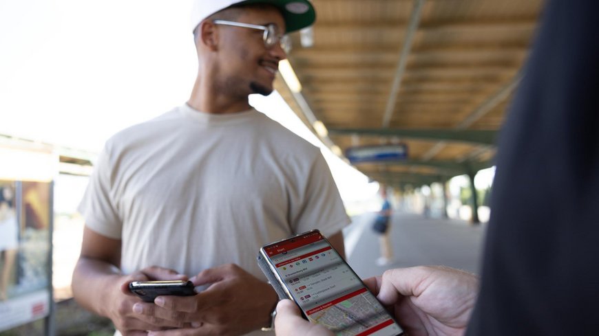 Foto von Person am Bahnhof, die Smartphone mit geöffneter Fahrinfo in der Hand hält 