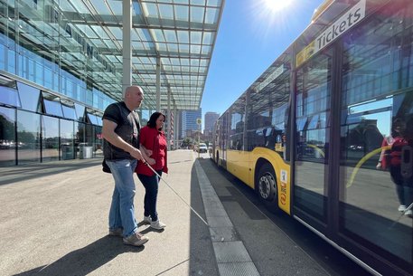 Mitarbeiterin hilft seheingeschränktem Fahrgast beim Einstieg in den Bus