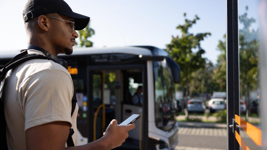Ein Mann steht vor einem Bus und hält ein Handy in der Hand