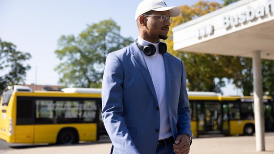 Aufnahme eines jungen Mannes, der sich auf einem Busbahnhof befindet. Im Hintergrund ein Bus.